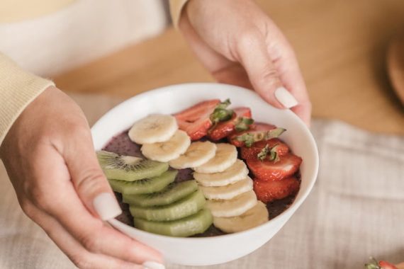 Delicious smoothie bowl topped with fresh fruits like kiwi, banana, and strawberries, held by manicured hands.