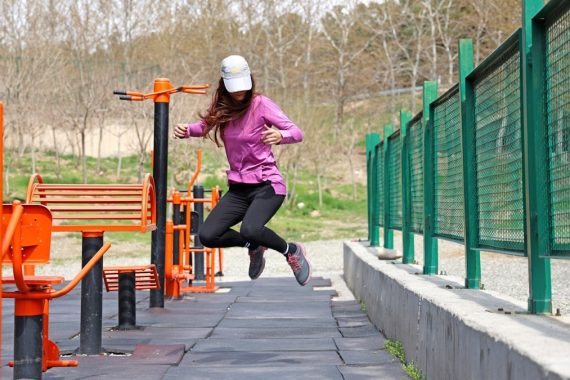 A young female model wearing sportswear is jumping in the air at a park's sports area. The photo is captured with a high shutter speed.